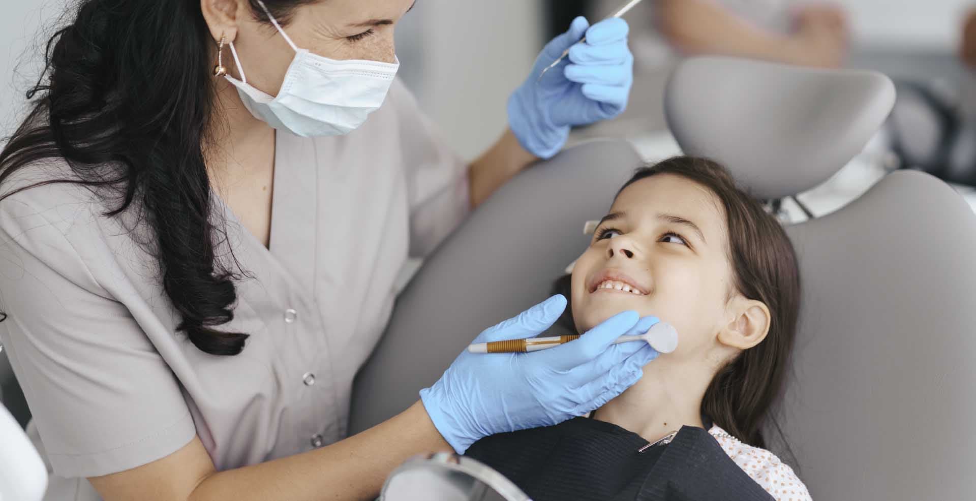 Niña sonriendo en el sillón dental, junto a la dentista